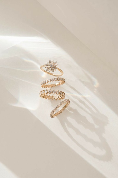 A refined product hero shot featuring four gold rings stacked vertically against a neutral background with soft, diffused sunlight casting delicate shadows.