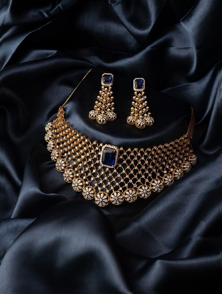 A high-end product photography shot of a gold and sapphire necklace set resting on dark, flowing silk fabric.