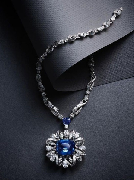 A high-end, minimalist studio photograph featuring a sapphire and diamond necklace against a textured dark backdrop to emphasize luxury and texture.