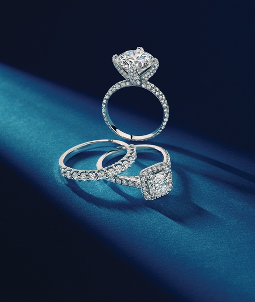 A high-end product shot featuring three diamond rings arranged on a deep blue silk surface with focused studio lighting.