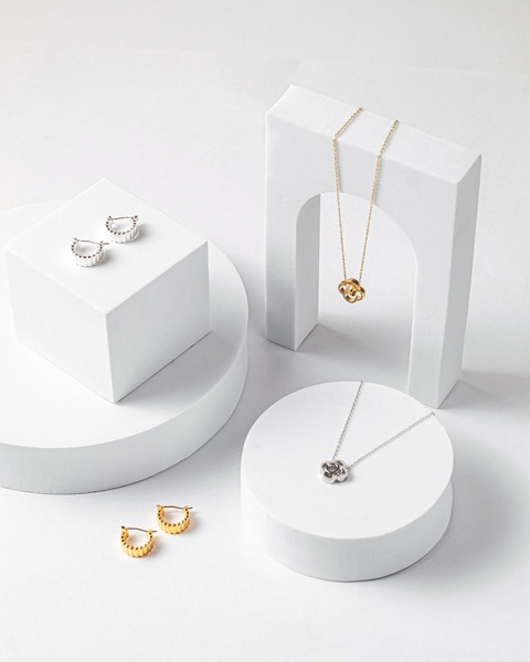A sophisticated still life photography composition featuring jewelry displayed on white geometric platforms to convey a premium, clean aesthetic.