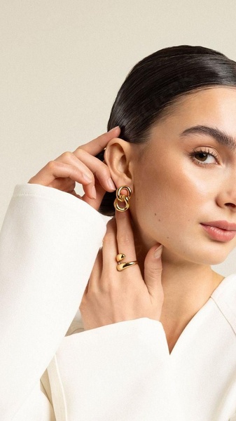 A refined lifestyle shot focusing on a model wearing elegant gold earrings and a matching ring, utilizing clean backgrounds to highlight product detail.