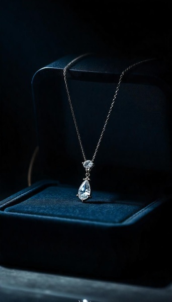 A refined, high-contrast close-up of a teardrop-shaped diamond necklace resting inside a dark blue velvet jewelry box, illuminated with soft directional light.