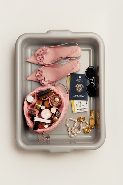 A top-down, structured product flat lay showcasing a travel organizer bag filled with essential items alongside elegant shoes, a passport, and accessories.