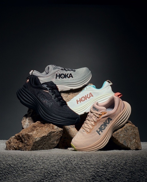 A high-quality studio shot of four different colorways of a running shoe resting on natural rocks against a dark background.