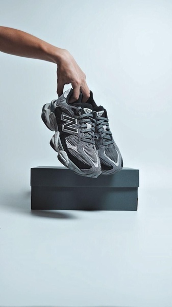 A high-contrast, studio-style product shot featuring a running shoe being held above its box against a clean, neutral background.