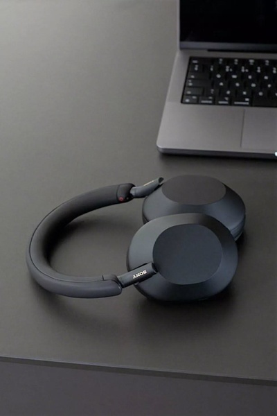 A high-end, top-down view of premium wireless headphones resting on a dark, minimalist desk alongside a laptop.