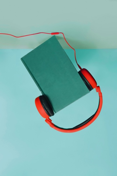 A high-contrast, studio-style shot featuring a green book suspended with red headphones against a matching pastel background.