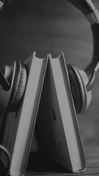 A high-contrast black and white composition featuring an open book with headphones draped over it, emphasizing a clean, intellectual product aesthetic.