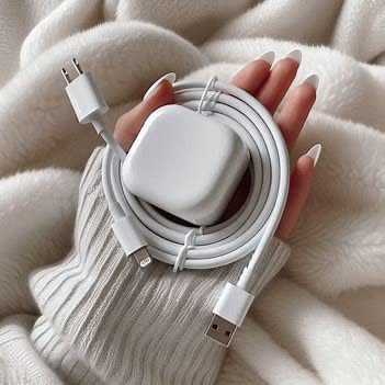 A close-up photograph showcasing a white USB-C charger and coiled cable held in a hand against a soft, plush white background.