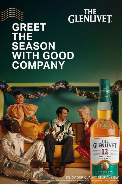 A lifestyle-focused creative featuring a group of friends socializing in a warm, festive living room setting with a bottle of single malt scotch whisky as the centerpiece.