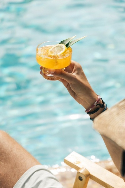 A close-up, sun-drenched shot of a hand holding a refreshing citrus cocktail by a pool, emphasizing a vacation lifestyle.
