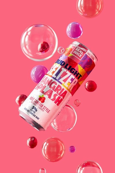 A high-energy, vibrant product hero shot featuring a hard seltzer can surrounded by floating fruit and bubbles against a pink background.