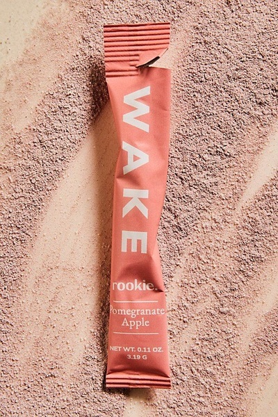 A close-up vertical shot featuring a single product stick of Pomegranate Apple powder against a textured backdrop of the same ingredient dust.