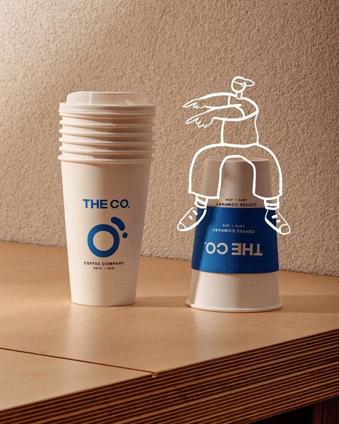 A creative product hero shot featuring a branded coffee cup paired with a playful, hand-drawn character illustration.