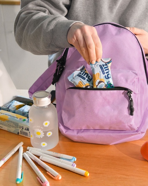 An authentic, relatable close-up showing a hand placing a branded energy bar into a backpack, signaling convenience and on-the-go lifestyle benefits.