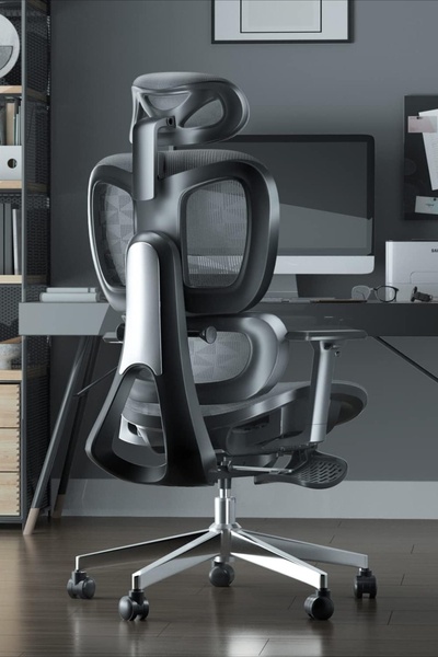 A high-quality, studio-lit photograph showcasing an ergonomic office chair from a rear-angle view in a modern, organized workspace.