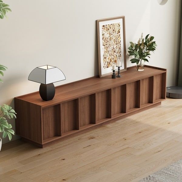 A high-quality, eye-level product shot of a low-profile walnut TV stand styled in a clean, minimalist home interior.