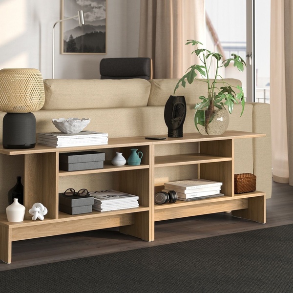 A high-quality lifestyle shot featuring a wooden console table styled with decorative items and books, positioned behind a sofa in a bright, modern living room.