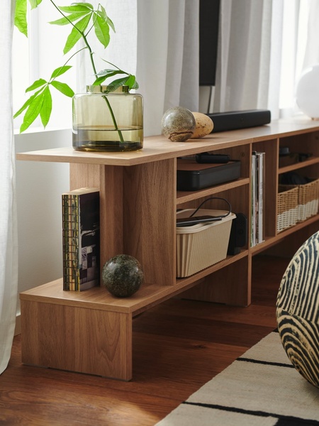 A high-end media console featuring natural wood grain, decorated with a glass vase and botanical accents to evoke a serene, aspirational home environment.