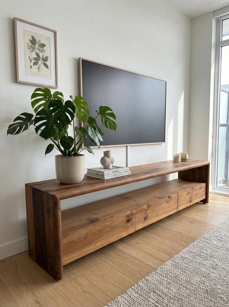 A high-quality lifestyle shot featuring a wooden media console, a monstera plant, and a mounted TV in a bright, modern living room.