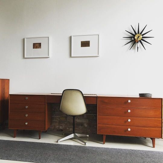 A high-quality, balanced wide shot of a teak mid-century desk paired with a minimalist chair, featuring stylized wall decor.