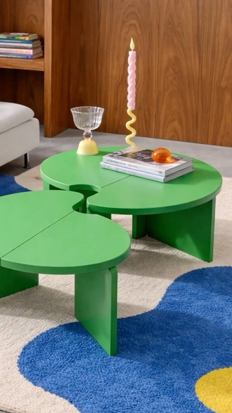 A high-angle product shot of a unique, clover-shaped green coffee table paired with curated decorative objects on a textured rug.