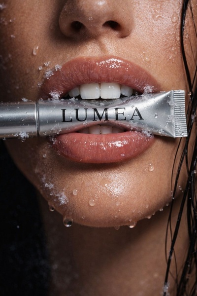 A high-fashion close-up shot featuring a model biting a silver tube, with ice crystals and water droplets accentuating the product texture.