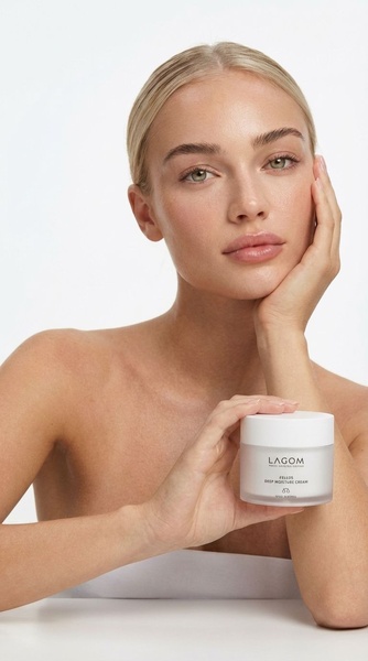A high-end, clean-aesthetic studio shot featuring a model holding the deep moisture cream close to her face to highlight skin hydration.