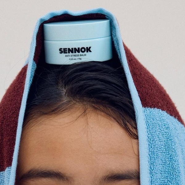 A close-up, high-contrast portrait featuring an anti stress balm resting on a person's head, wrapped in a simple towel.
