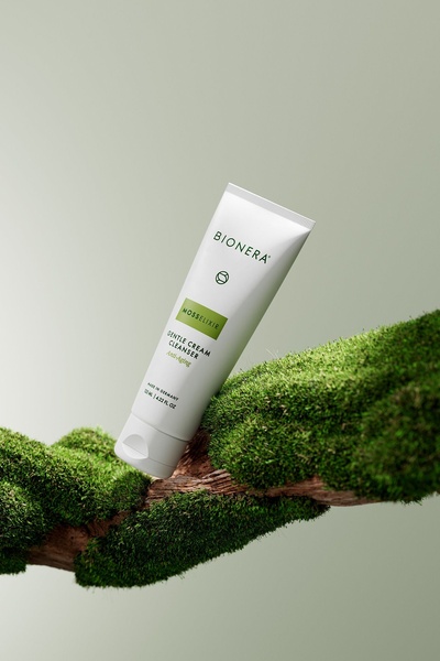 A high-end skincare product is displayed resting on a mossy branch, emphasizing natural ingredients and a clean, organic aesthetic.
