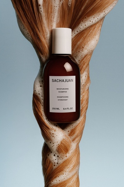 A high-end product photography shot featuring a shampoo bottle twisted into a strand of hair with soap suds, emphasizing hydration.