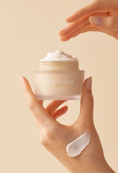A close-up, high-end product photography shot showcasing the texture and application of a ferment cream on a hand against a neutral background.