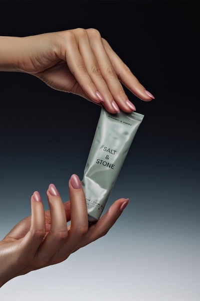 A close-up studio shot featuring hands delicately holding a tube of hand cream against a stark, high-contrast background.