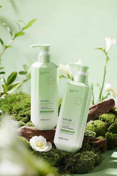 Two bottles of shampoo displayed on a mossy, woodland-themed surface, surrounded by lush greenery and delicate white flowers.
