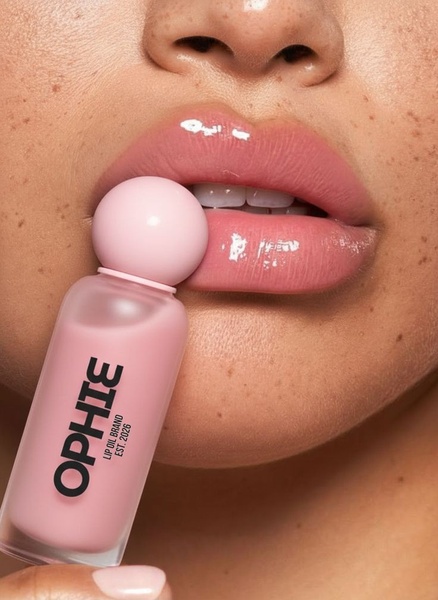 A close-up aesthetic shot of a lip oil bottle held against a model's lips to highlight product texture and shine.