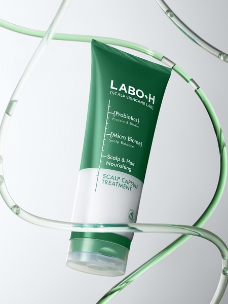 A high-end, clean studio shot of a Scalp Capsule Treatment tube suspended in a stylized water-tube frame, emphasizing ingredient purity and clinical focus.