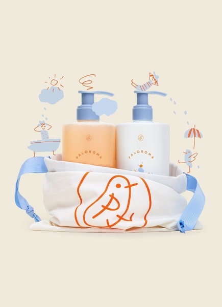 A high-quality product shot of two body lotion bottles placed inside a branded fabric bag, surrounded by whimsical, hand-drawn line illustrations.