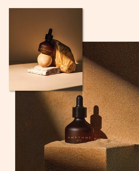 A minimalist, high-end product photography shot featuring a serum dropper bottle set against natural textures and earth-toned geometric blocks.