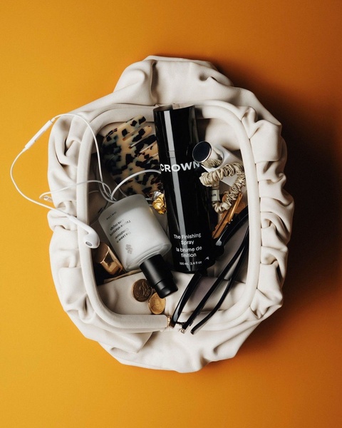 An organized overhead flat lay composition showcasing hair care products, styling tools, and personal accessories on a warm orange background.