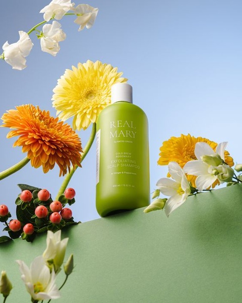A minimalist, high-contrast product photography shot featuring a bottle of exfoliating scalp shampoo surrounded by vibrant flowers and botanical elements.