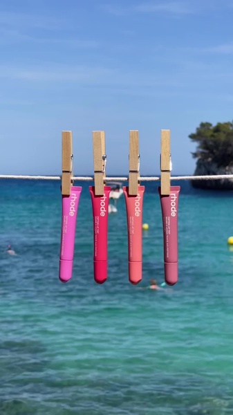 A bright, sunny shot of four different colored lip tints hanging from a clothesline over a clear blue ocean background.
