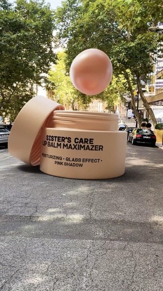 A giant 3D-rendered lip balm jar sits on a realistic city street, creating a surreal and high-impact hero product display.