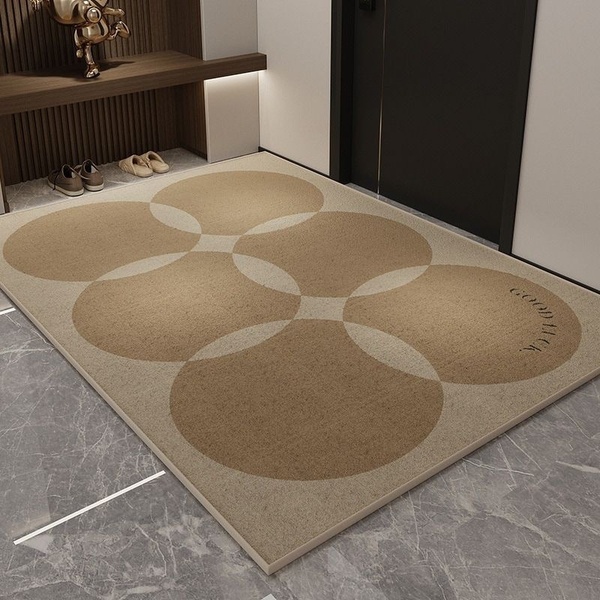 A high-angle product photograph of a circular-patterned floor mat in a neutral beige palette, showcased in a modern entryway.