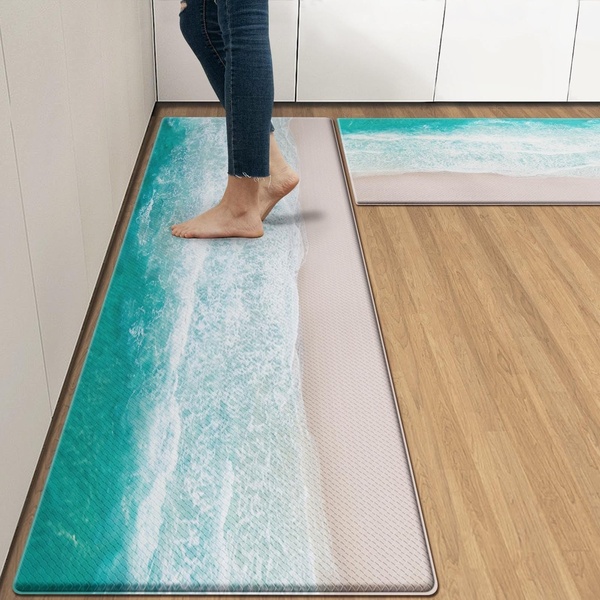 A high-angle product shot displaying a comfortable, coastal-themed floor mat in a modern kitchen setting, showing its texture and placement.