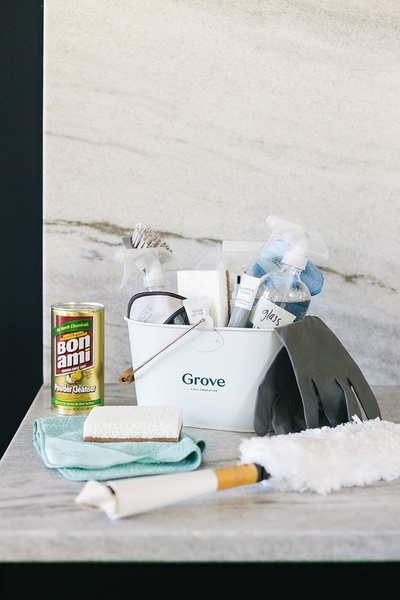 A high-end, top-down product hero shot showcasing a curated basket of cleaning supplies, including microfiber cloths, sprays, and specialized cleaners.
