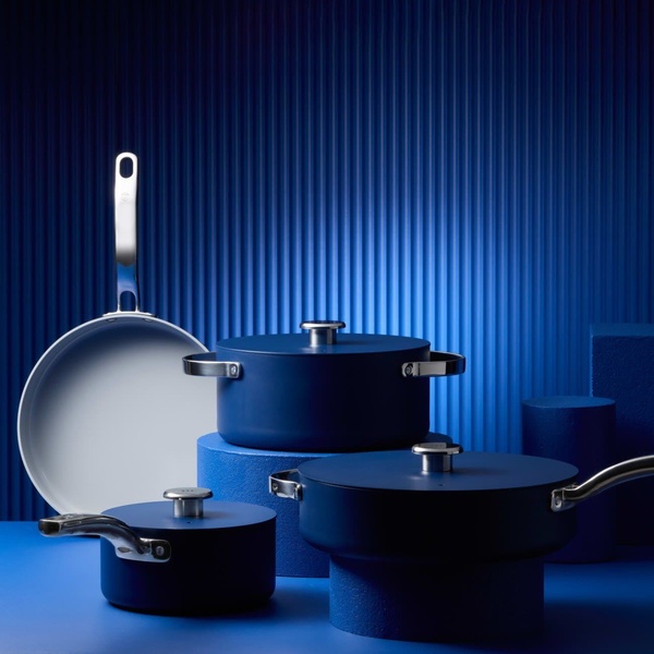 A high-end cookware set is displayed in various shades of blue on matching pedestals, creating a bold, monochromatic visual impact.