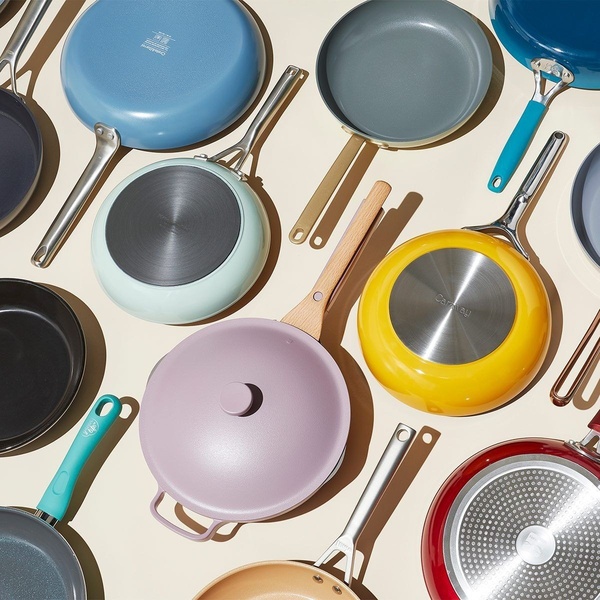 A high-angle, organized flat-lay shot showcasing a collection of modern, colorful non-stick cookware pieces on a neutral background.