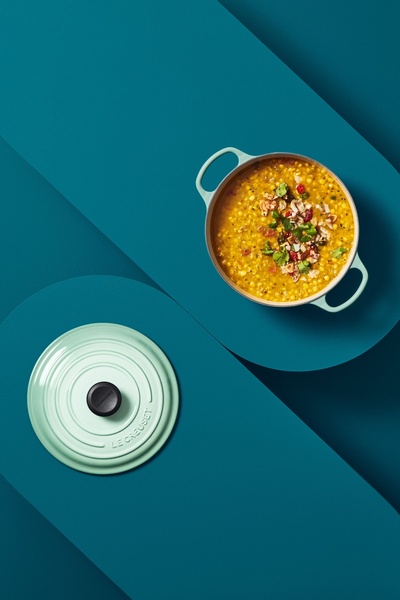 A high-angle, top-down shot of a mint-colored enameled dutch oven and its lid, symmetrically balanced against a deep teal background.
