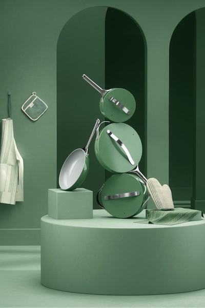 A high-end, color-coordinated stack of non-stick cookware displayed on a podium within a minimalist architectural setting.